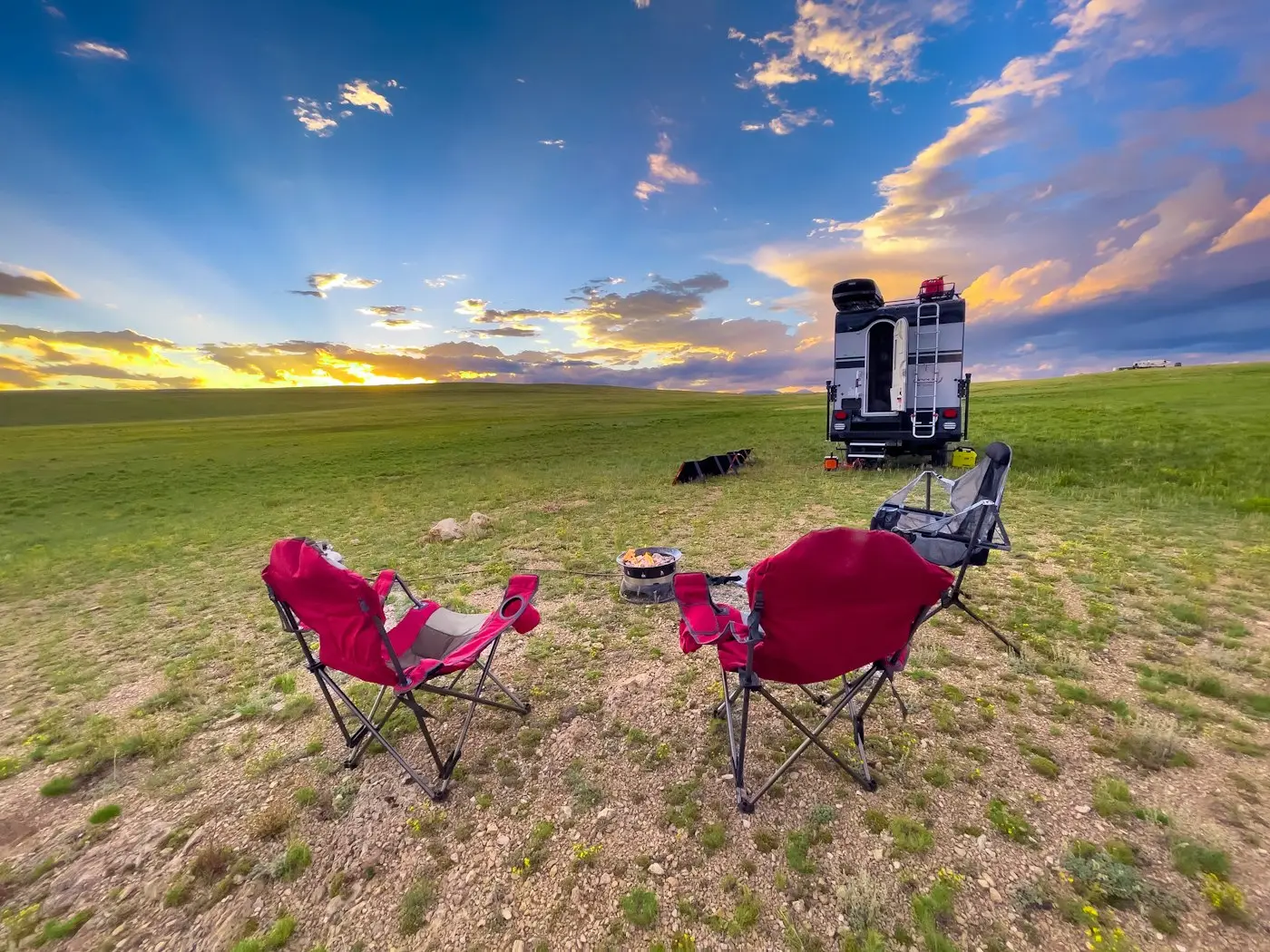 Camp chairs around a fire pit beside an RV at sunset